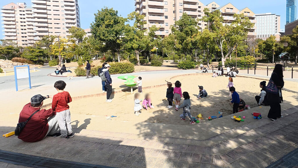 都会のビル群に囲まれた百道中央公園の広々とした砂場エリア