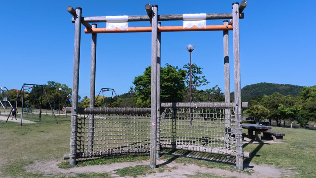 今津運動公園のアスレチック広場にある「ウェブアドベンチャー」。木製の高い柱の間に張られた、垂直のネットを登って遊ぶアスレチック遊具。