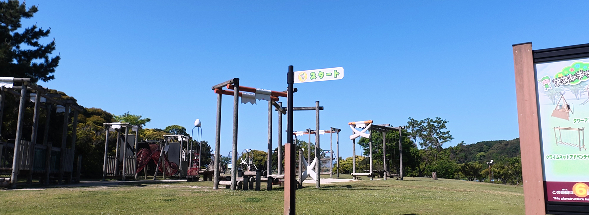 今津運動公園のアスレチック広場。木製遊具の並ぶコースの「スタート」看板と青空。