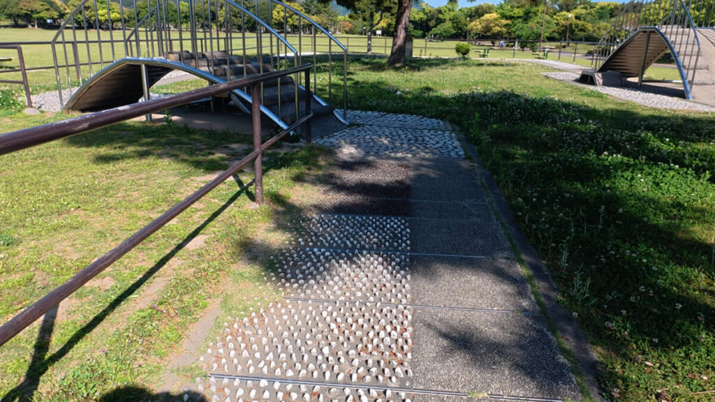 今津運動公園のリフレッシュロード。手前に白く突起した「とがった石（Cエリア）」が敷き詰められた歩道と、奥に続く手すり付きの木製の橋（Bエリア）。