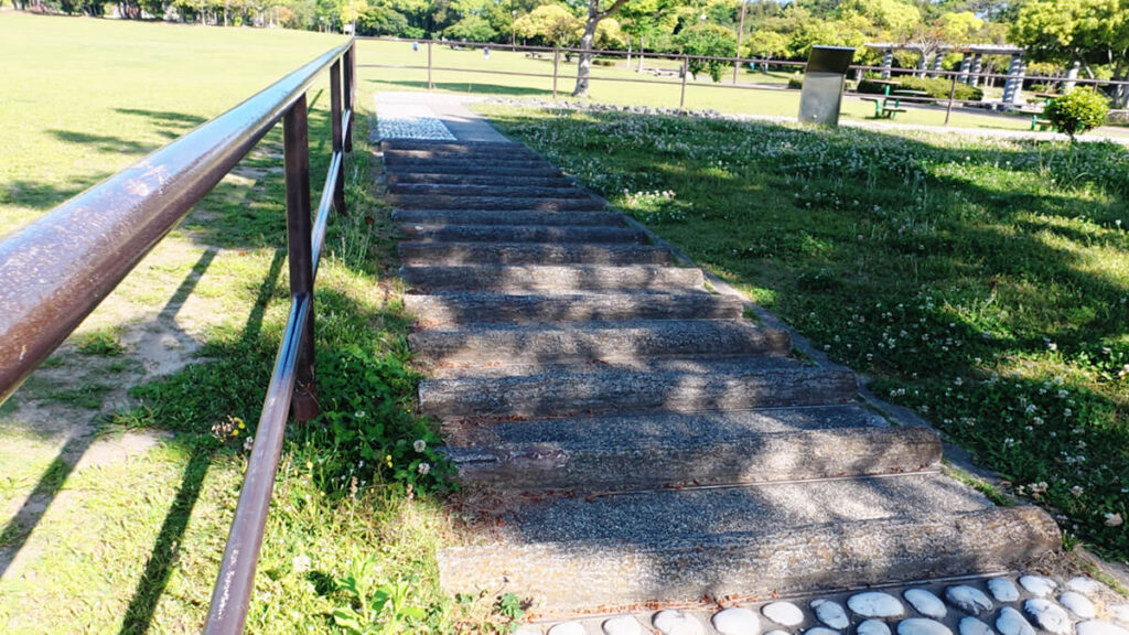 今津運動公園のリフレッシュロードにある、丸太を横向きに並べたようなデザインの緩やかな坂（Bエリア・橋の部分）。左側には黒い手すりが設置されている。