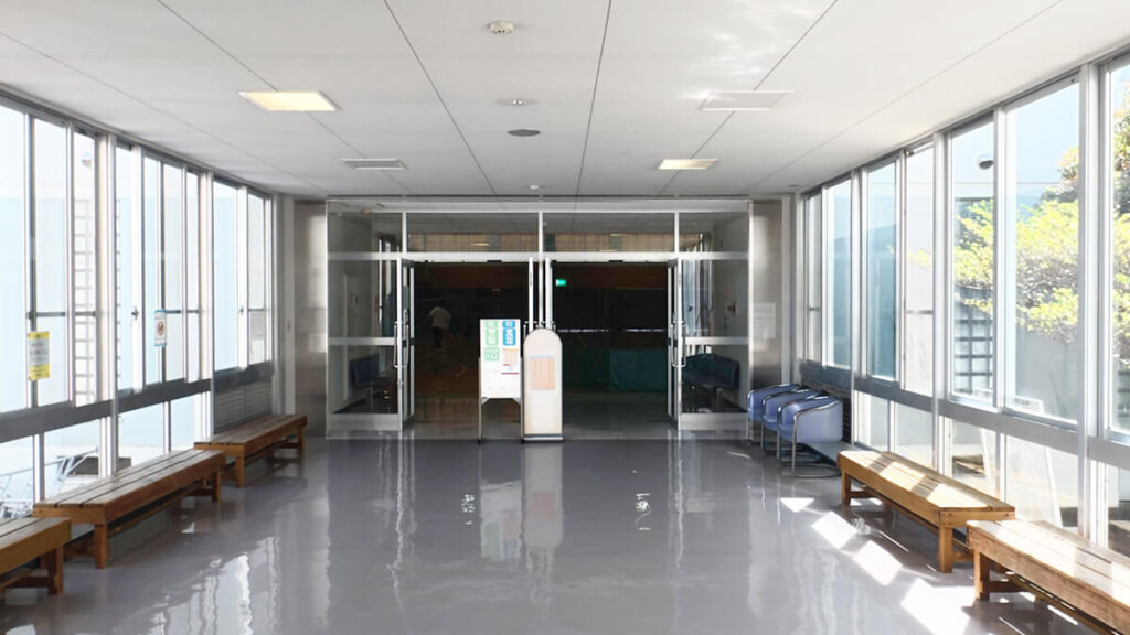 今津運動公園体育館の競技場入り口へと続く明るいロビー通路。左右の窓沿いに木製ベンチが設置されている。