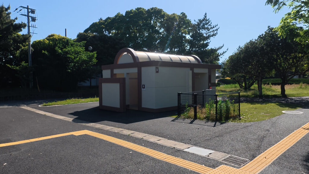 今津運動公園の第2駐車場および管理棟南側にある公衆トイレ外観。ベージュの壁に半円形の屋根が特徴的な建物。