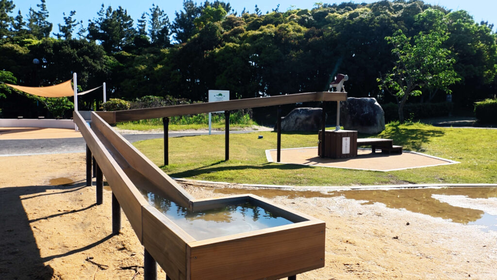 今津運動公園にある木製のせせらぎ水路。給水ポンプから流れた水が緩やかな傾斜を伝って下流へ流れる仕組みの遊具。