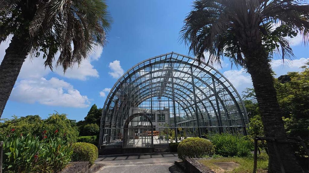 花畑園芸公園にあるアーチ形のガラス温室と、入口の両側に立つヤシの木