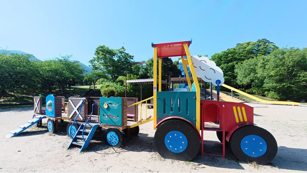 西油山中央公園の遊具広場にある、赤と青のカラフルな汽車の形をした幼児向けの複合遊具 。