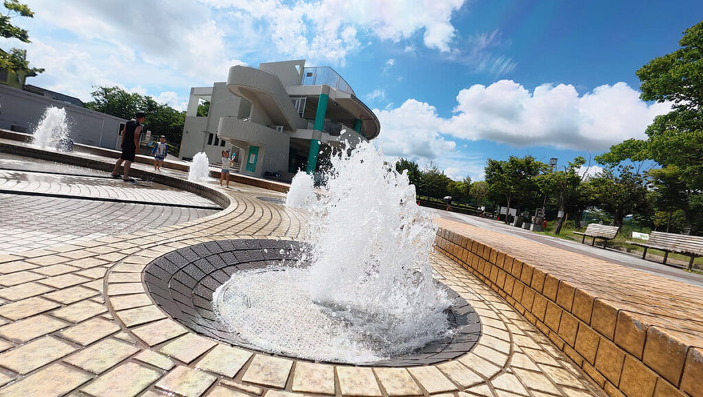 白水大池公園の噴水広場。建物を背景に噴水が上がる夏の水遊びエリア