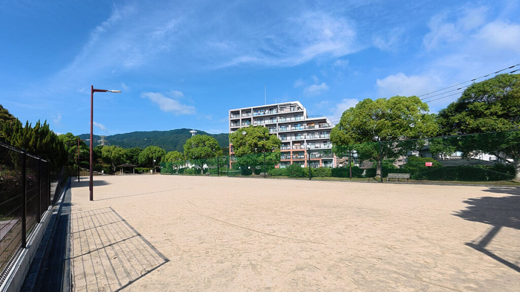 福岡市南区の桧原運動公園にある自由広場（北）の全景。フェンスに囲まれた広い土の広場で、開放感がある