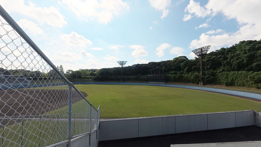 桧原運動公園の野球場の外野側。フェンス越しに芝生の外野と照明設備が見える