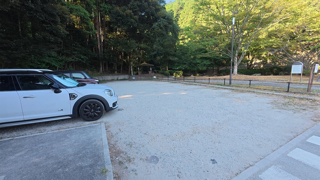 柏原公園の木々に囲まれた未舗装の駐車場と、駐車している複数の車