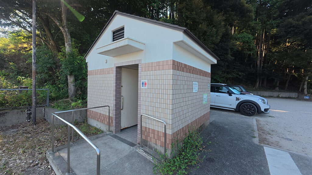 柏原公園の入口付近にある、男女共用の案内表示と手すり付き通路を備えた公衆トイレ